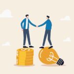 Idea pitching, fund raising and venture capital, selling business or merger agreement concept, entrepreneur businessman standing on lightbulb idea lamp shaking hands with VC on money coins stack.