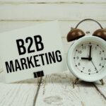 B2B Marketing text on paper card with alarm clock on wooden background