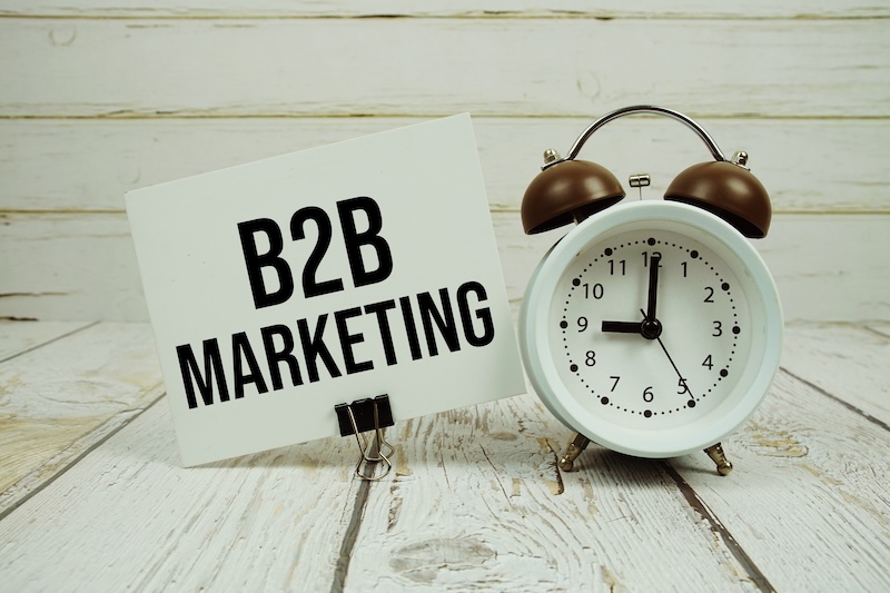 B2B Marketing text on paper card with alarm clock on wooden background