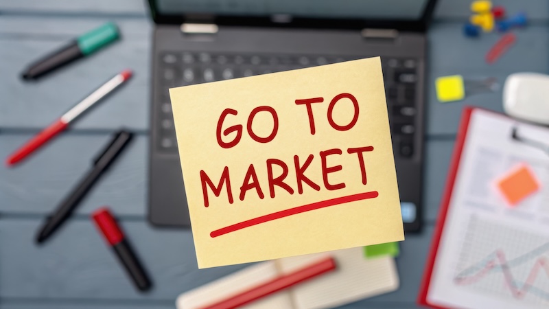 B2BMX GTM Strategy & Advanced ABM Track startup success execution competition goals concept. Sticky note with "Go to Market" on a desk with office supplies.