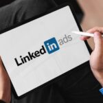 Dreamdata LinkedIn Benchmarks Report 2026 Person using tablet with linkedin ads logo