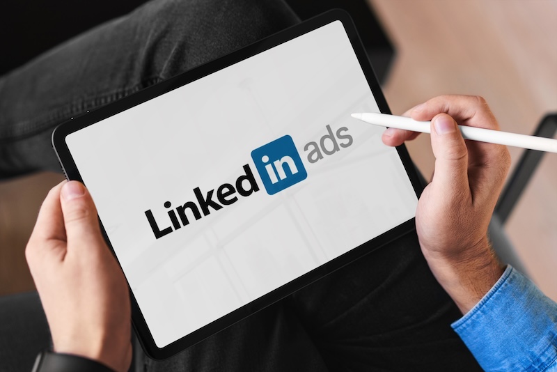 Dreamdata LinkedIn Benchmarks Report 2026 Person using tablet with linkedin ads logo