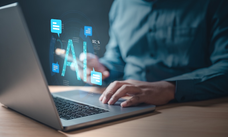 Demandbase AI A man is using a laptop with a blue screen chat bubble that has a blue word that says AI.